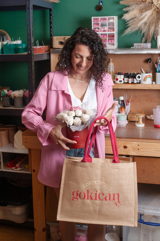 Woman holding a red bucket with flowers and a brown bag with 'gokican' branding in a workshop setting.