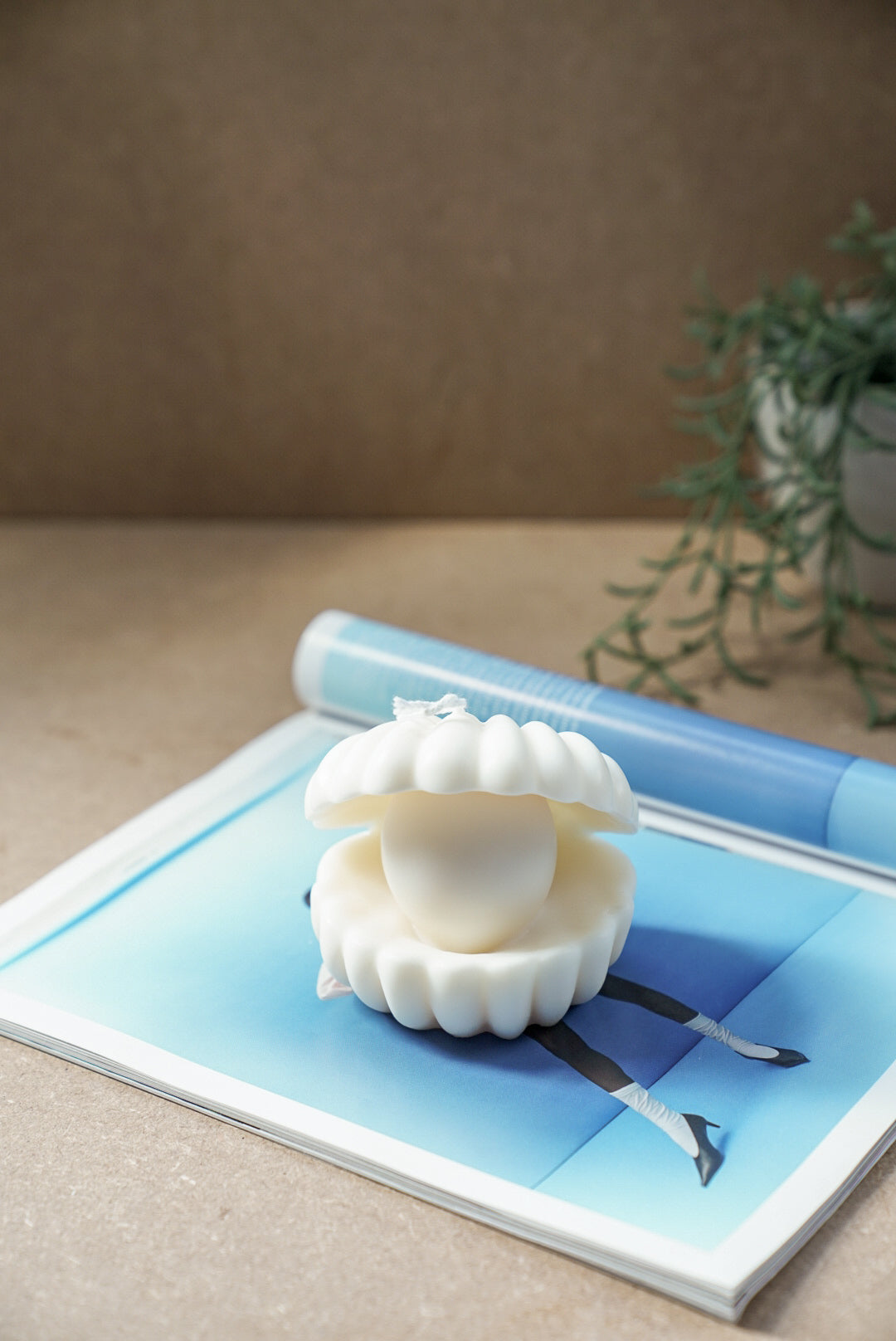 Large Clam Shell W/ Pearl Candle on a magazine with green plant on the background.
