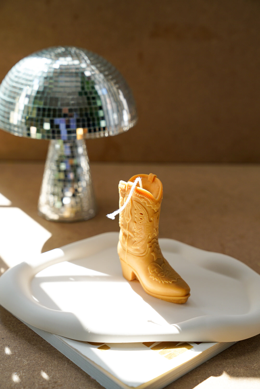 Brown Cowboy Boot Candle on a cloudy trinket tray with mushroom disco ball on the back.