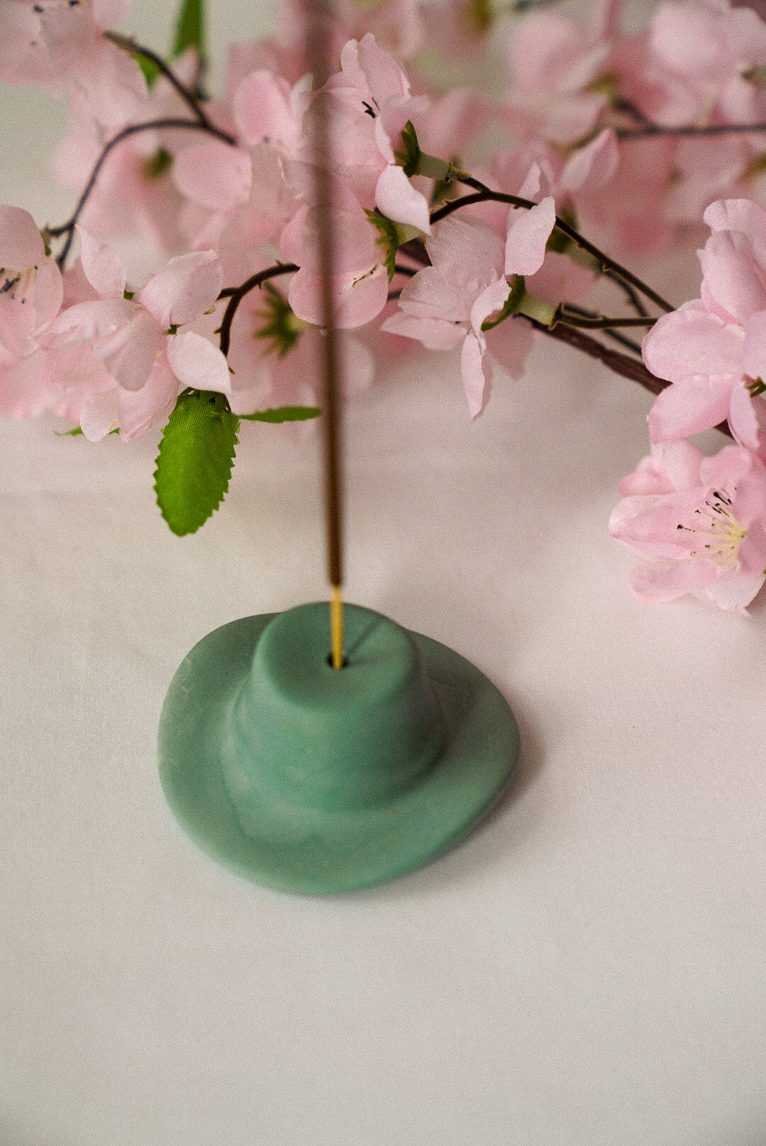 Zen Green Cowboy Hat Incense Holder with pink flowers on the background.