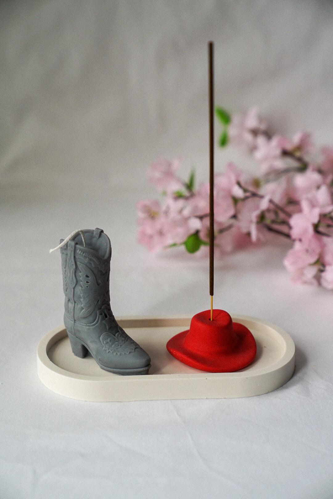 Grey Cowboy Boot Candle and Red Cowboy Hat Incense Holder on a trinket tray with flower background.