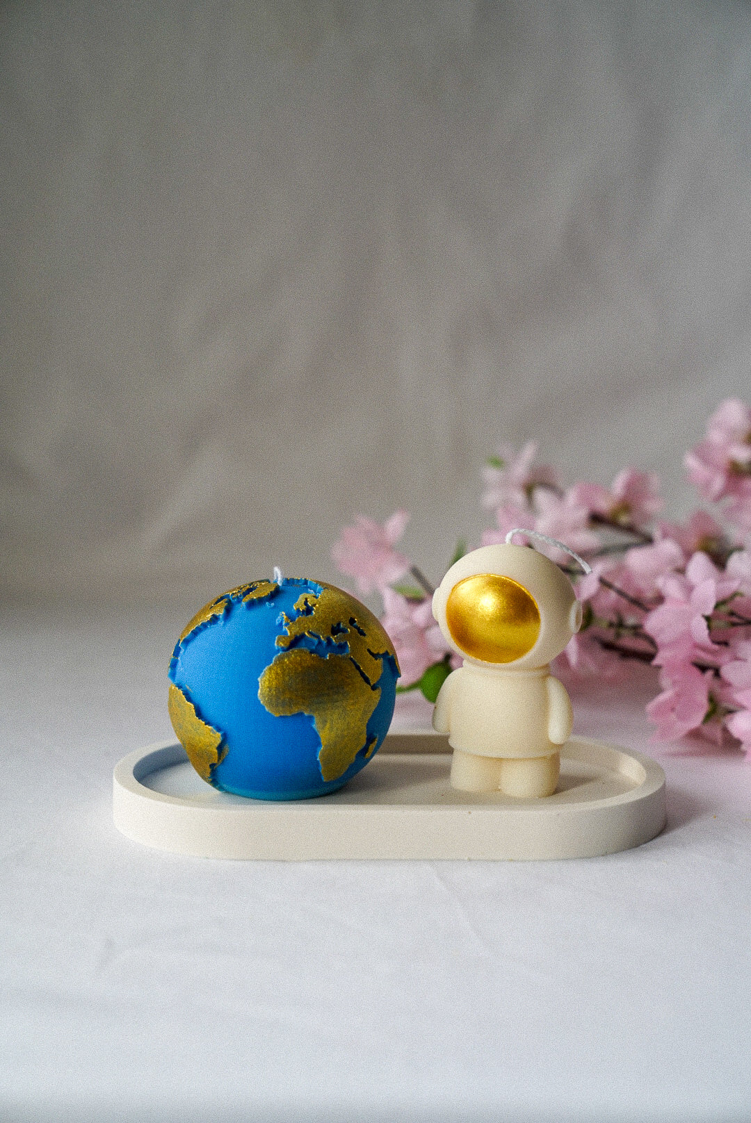 Ivory Space Man & Blue Globe Candle with gold painted on a white trinket dish with flowers on the background