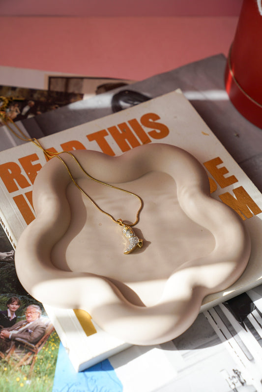Necklace on a wavy ceramic dish with a magazine underneath