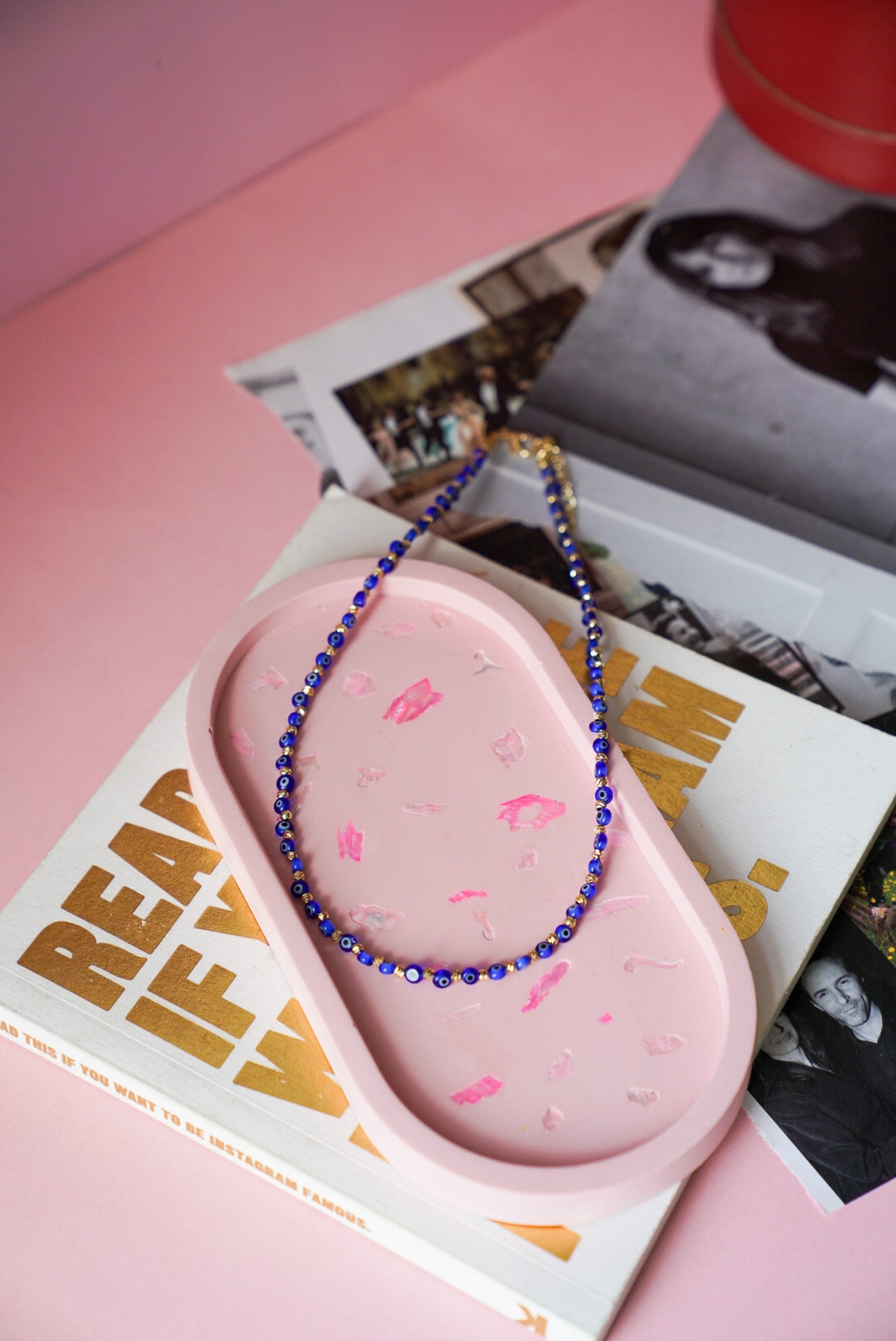 Pink silicone product with blue beaded necklace on a pink surface with magazine in background
