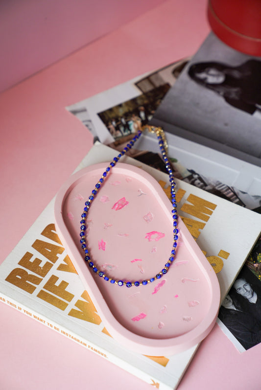 Pink silicone product with blue beaded necklace on a pink surface with magazine in background