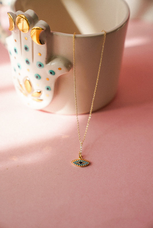 Necklace with a pendant on a pink surface next to a ceramic cup