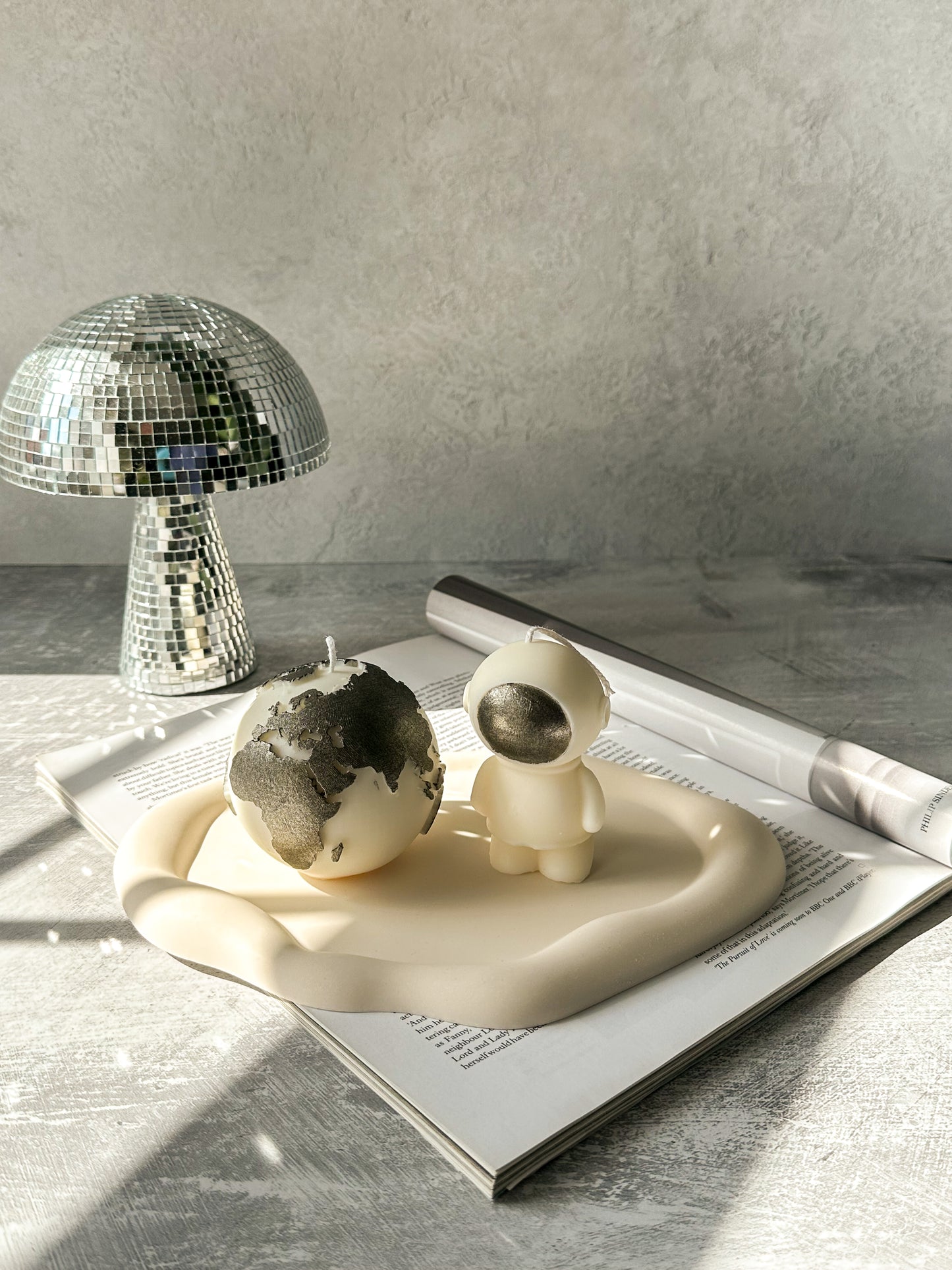Ivory Space Man & Globe Candle with silver painted on a off white trinket dish with grey background disco mushroom in the background
