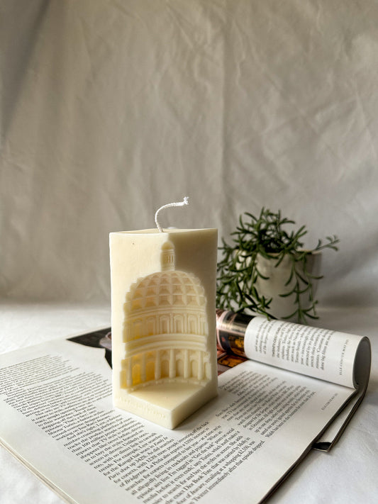 Ivory Rome Pantheon Capital Soy Candle on a magazine green plant on the background.