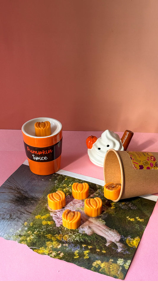 Cup with pumpkin spice flavor and small pumpkin decorations on a pink surface.