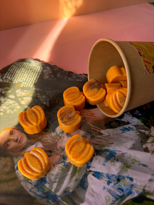Pumpkin shaped wax melts spilling out of a paper cup onto a magazine with a blurred background