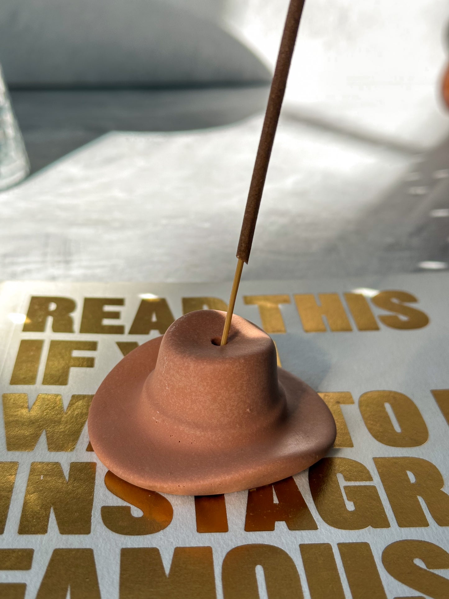 Terracotta Cowboy Hat Incense Holder with incense in it sitting on a book.