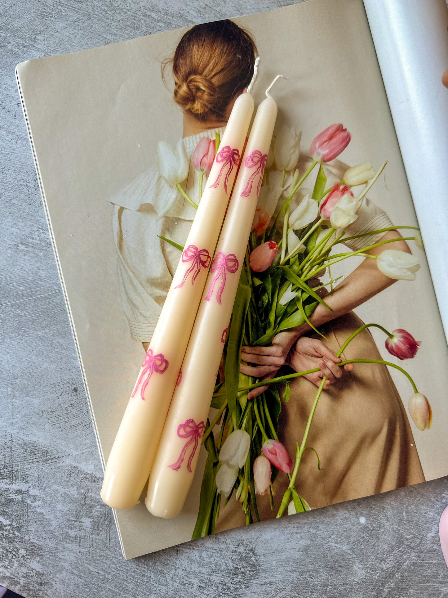 Pink Bow Hand-Painted Pillar Candles laying down on the magazine the lady holding tulips