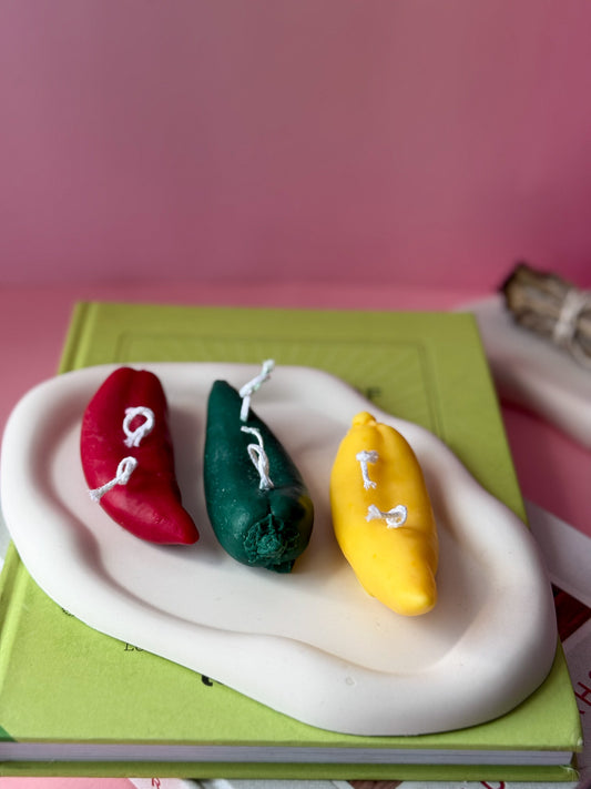 Three colourful chilie pappers on a white base with a pink background