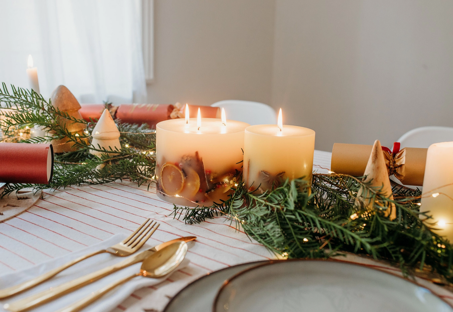 Decorative table setting with candles, greenery, and gold cutlery on a white tablecloth.