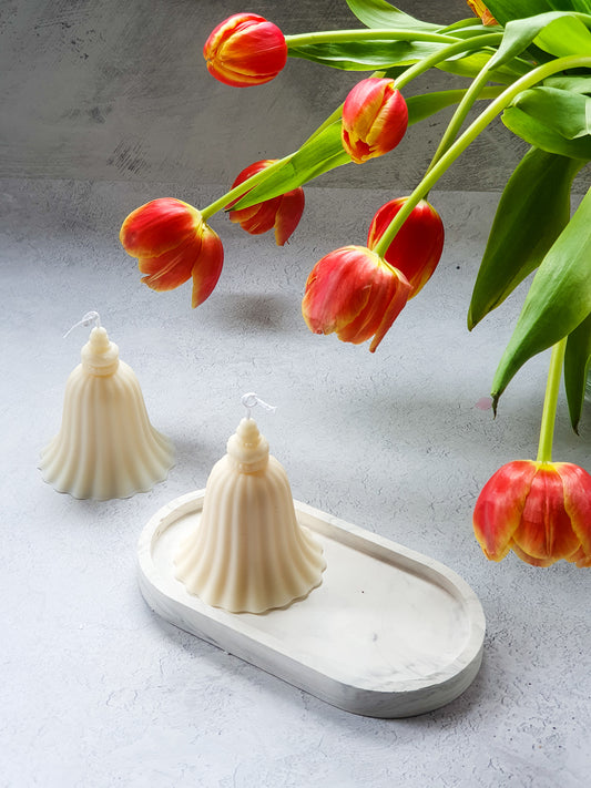 Two Ivory "Bell" shaped soy candle in a trinket dish with red tulips next to it