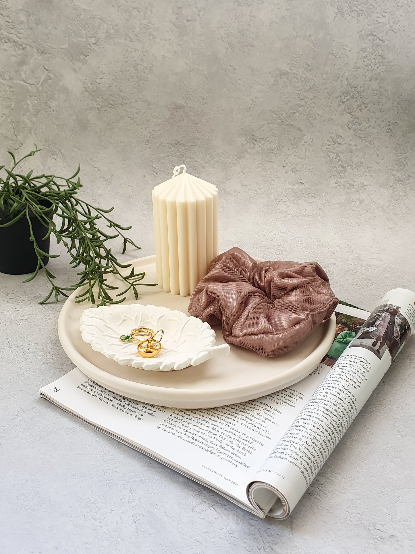Large Round Decorative Tray on a magazine on the tray there is a scrunchies, pillar candle and leaf shape trinket dish