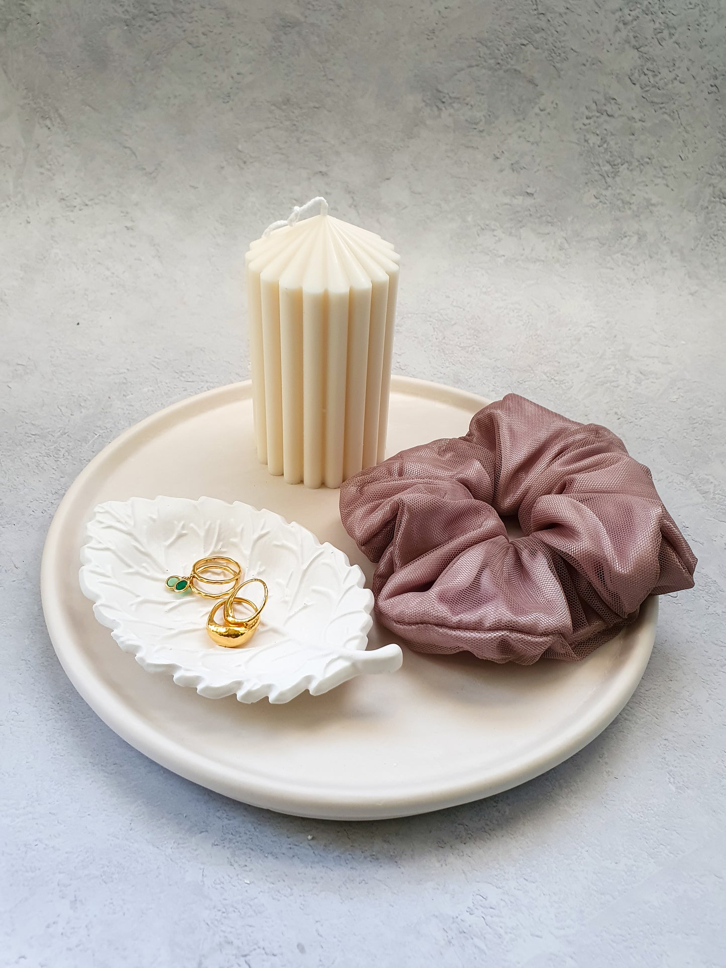 Large Round Decorative Tray on a magazine on the tray there is a scrunchies, pillar candle and leaf shape trinket dish