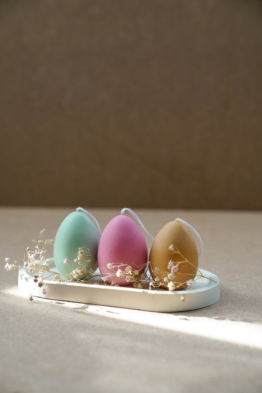 3 different colour Easter Egg Candles on a trinket dish with dry flowers around.