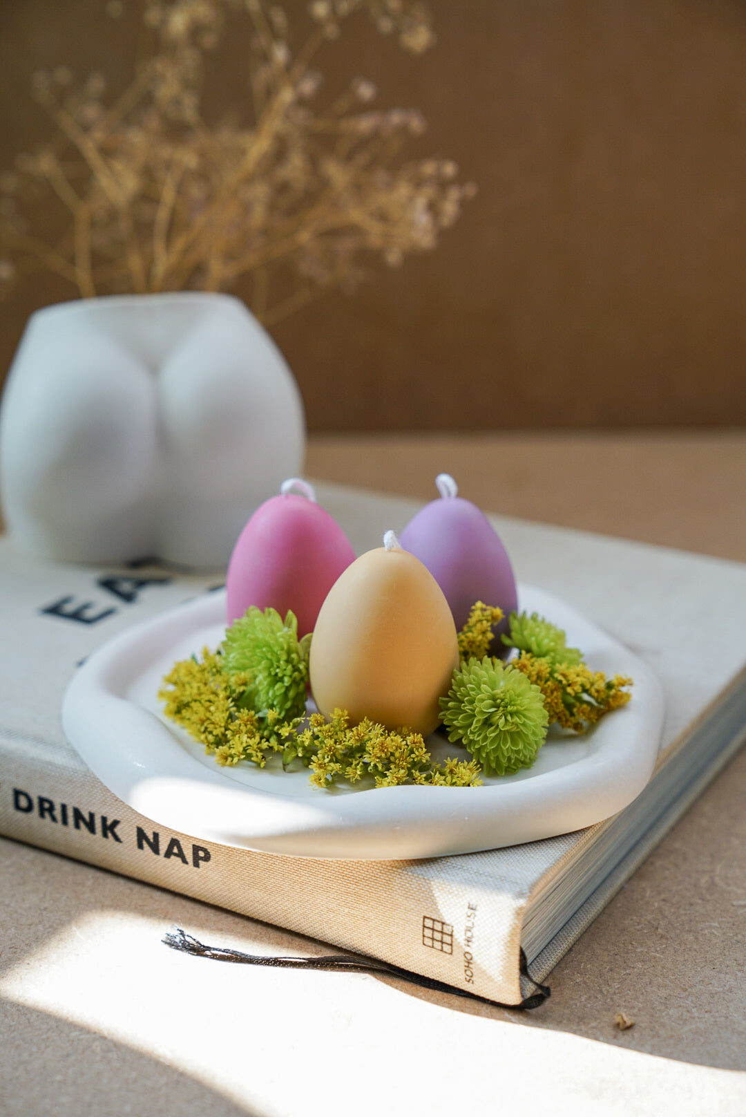 Easter Egg Candles on a trinket dish with green flowers around.