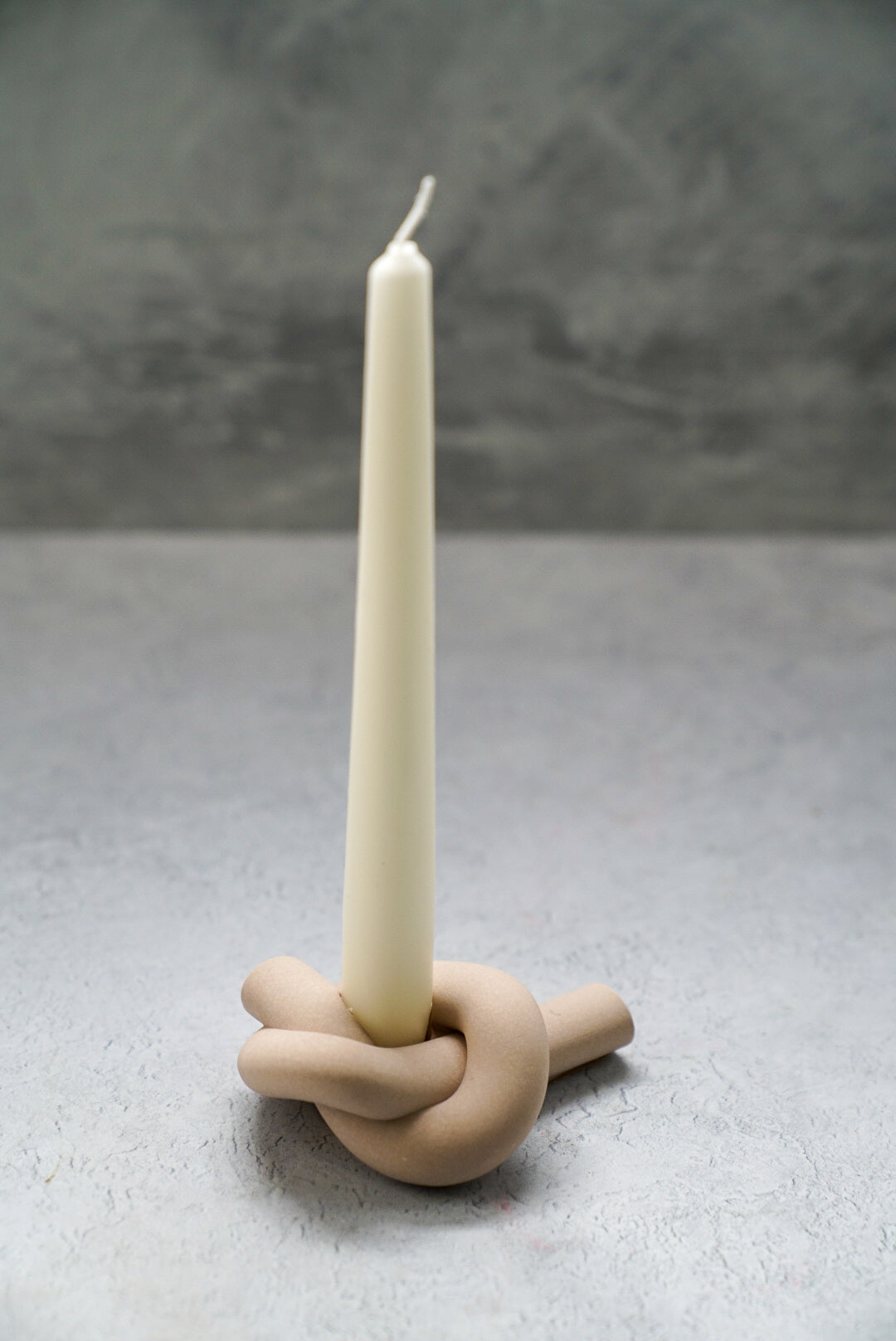 Latte colour Knot Shaped Candle Holder with long candle on it.
