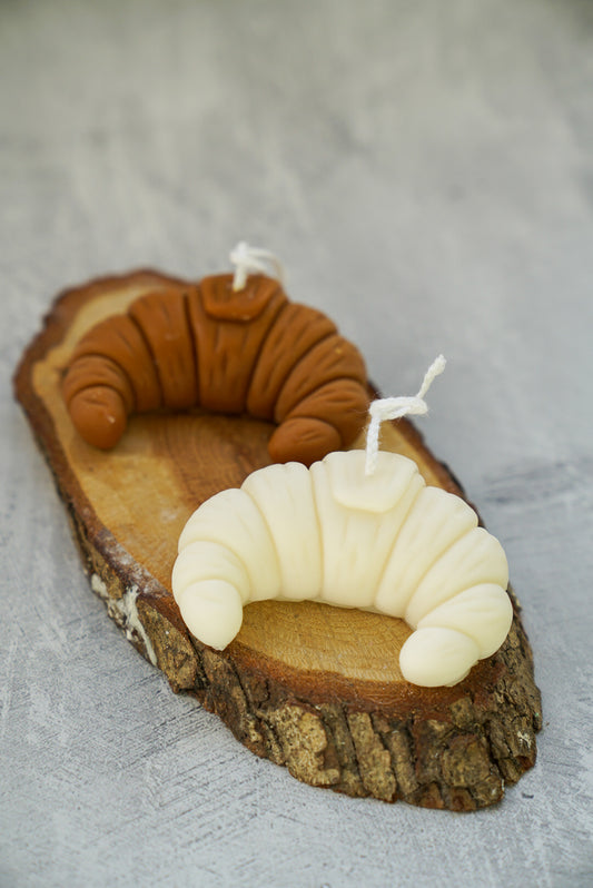 Brown an Ivory Croissant Shaped Candle on a wooden coaster.