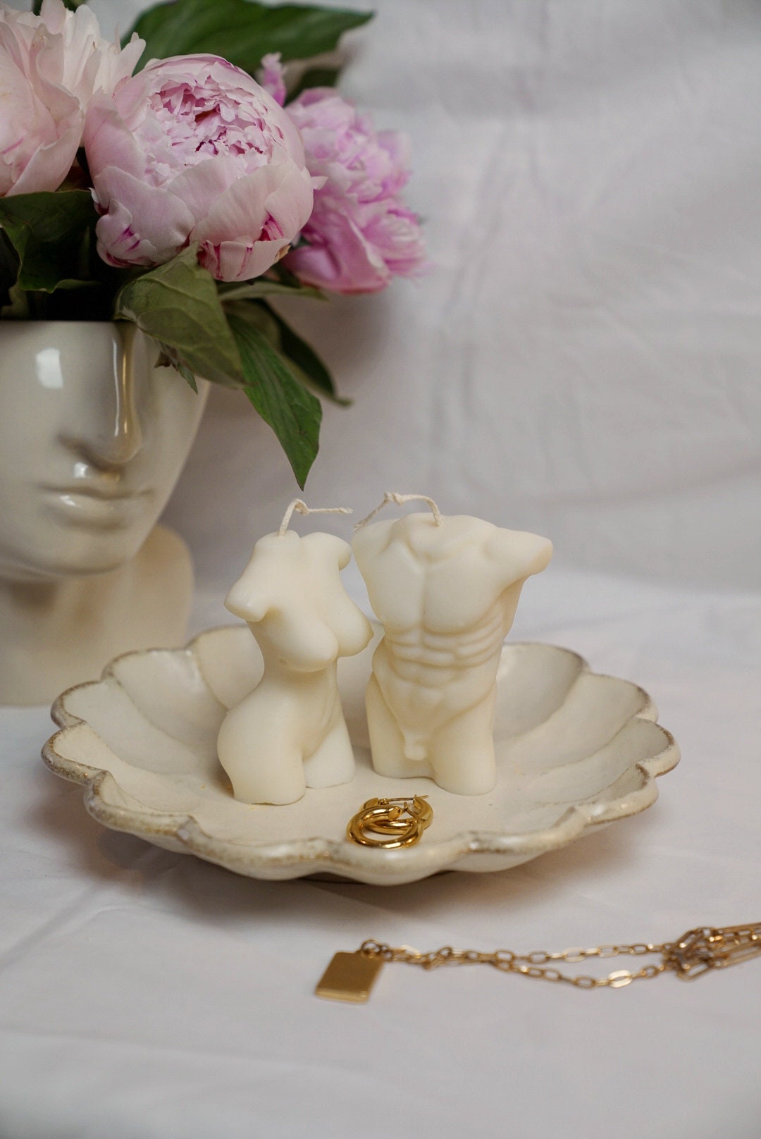 Male & Female Torso Candles on a flower shape plate with gold earring next to it.