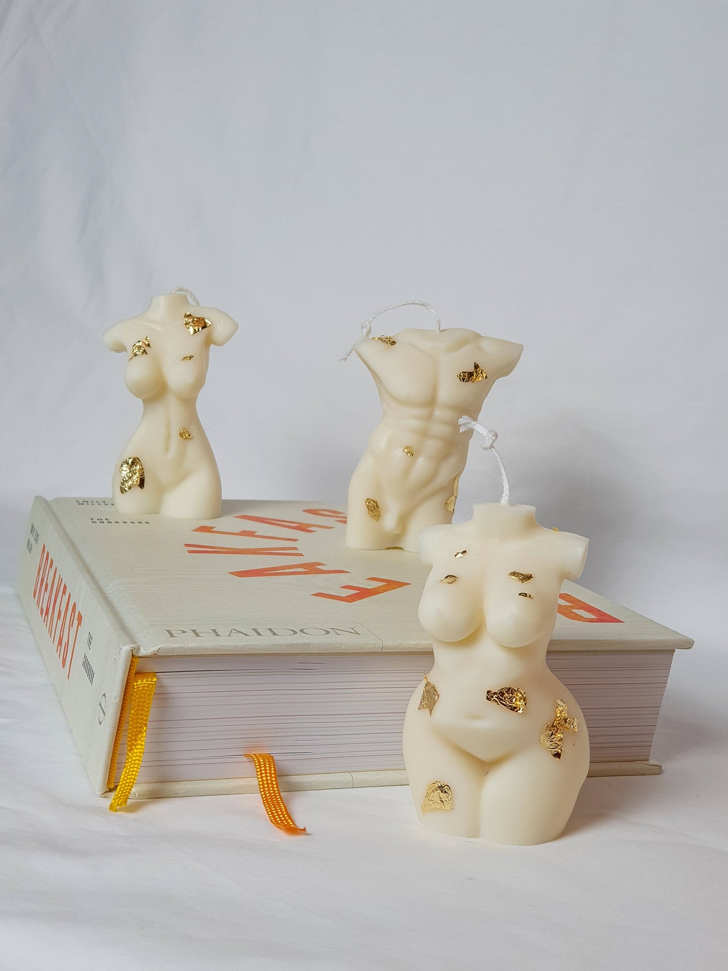 Curvy Goddess Candle with male and female body candles on a book with white background.
