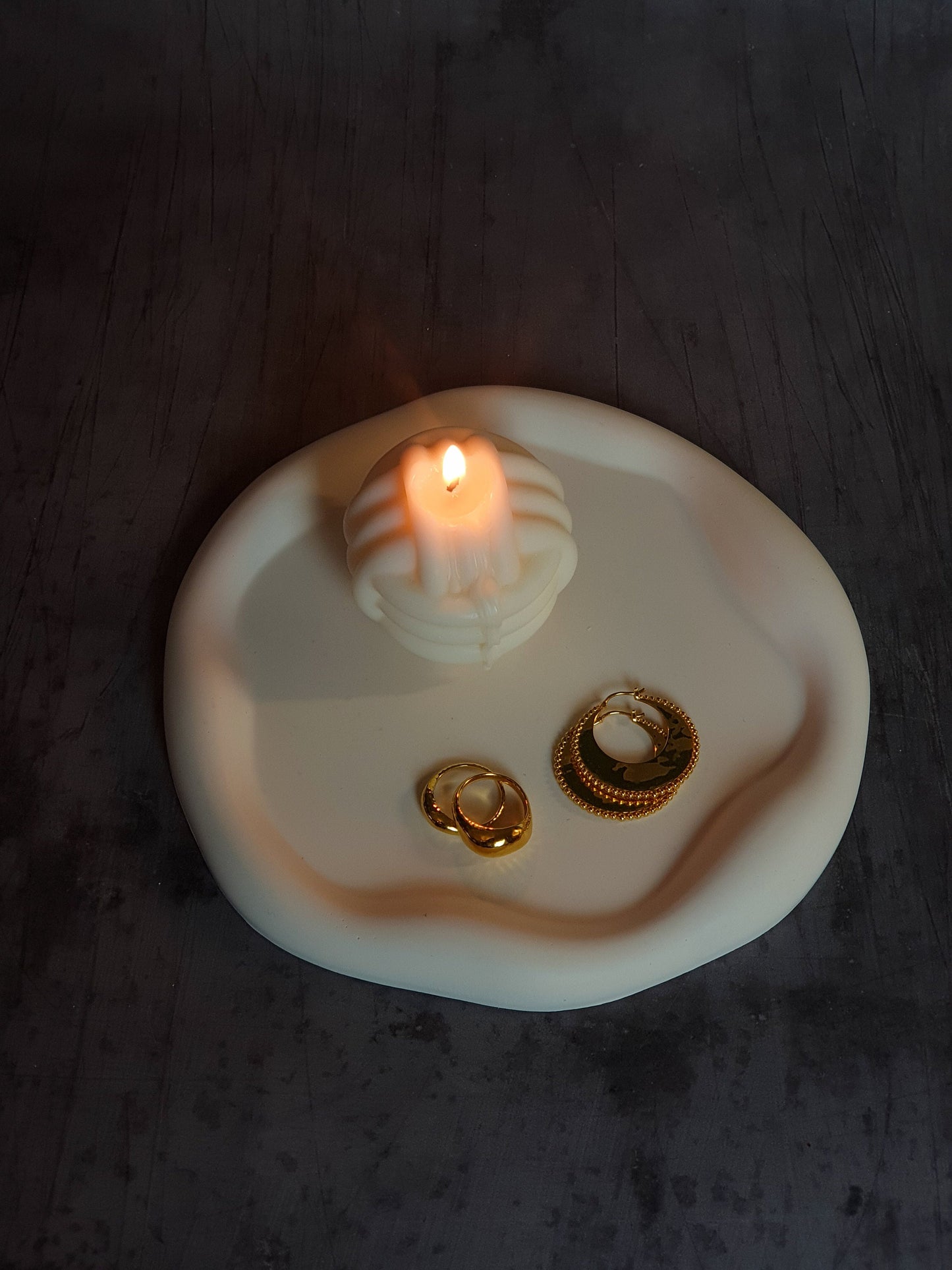 Curvy Round Trinket Tray with candle and jewellery on it with a grey background.