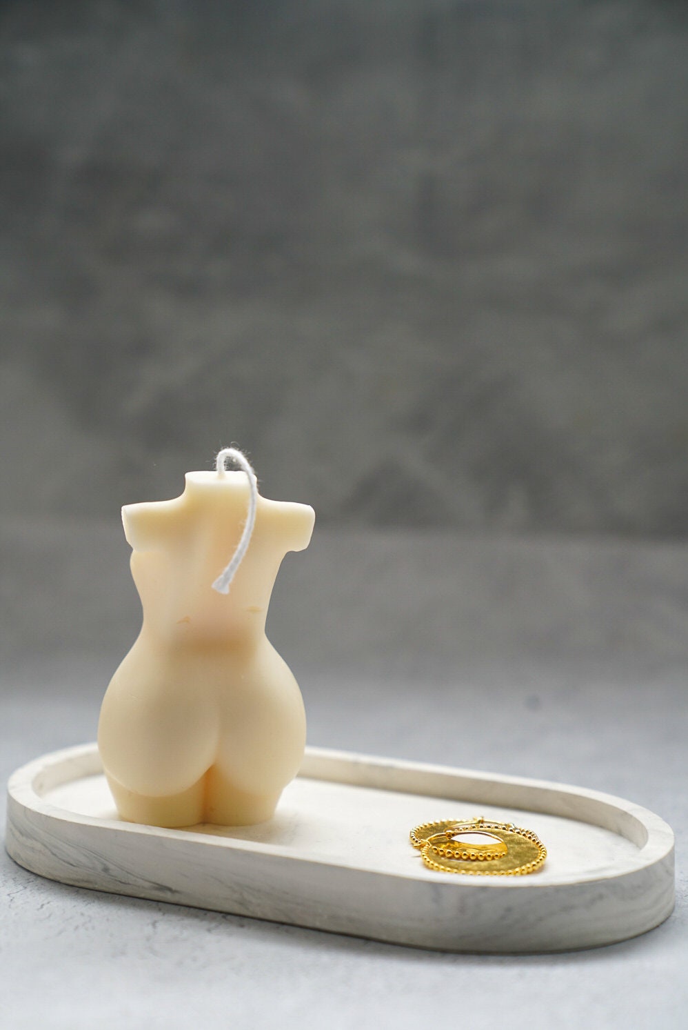Curvy Goddess Candle from the back on a trinket tray with gold earrings on it.