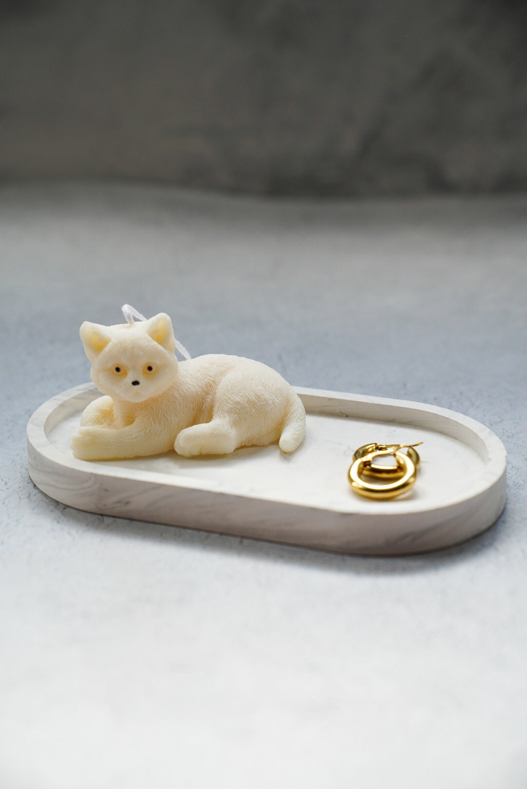 Cute Sitting Cat Candle is sitting on a oval trinket tray with gold earrings next to it.
