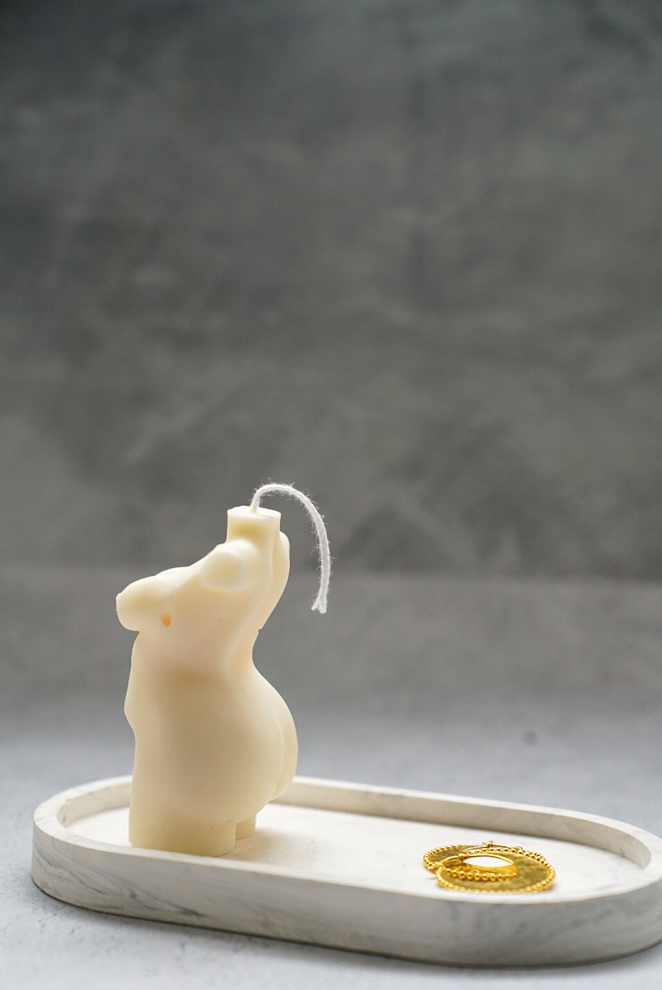 Curvy Goddess Candle from the side on a trinket tray with gold earrings on it.