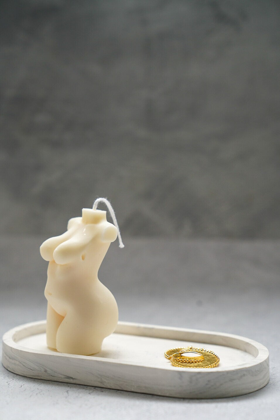 Curvy Goddess Candle from the side on a trinket tray with gold earrings on it.