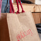 Jute bag with 'golican' branding held by a person in an indoor setting.
