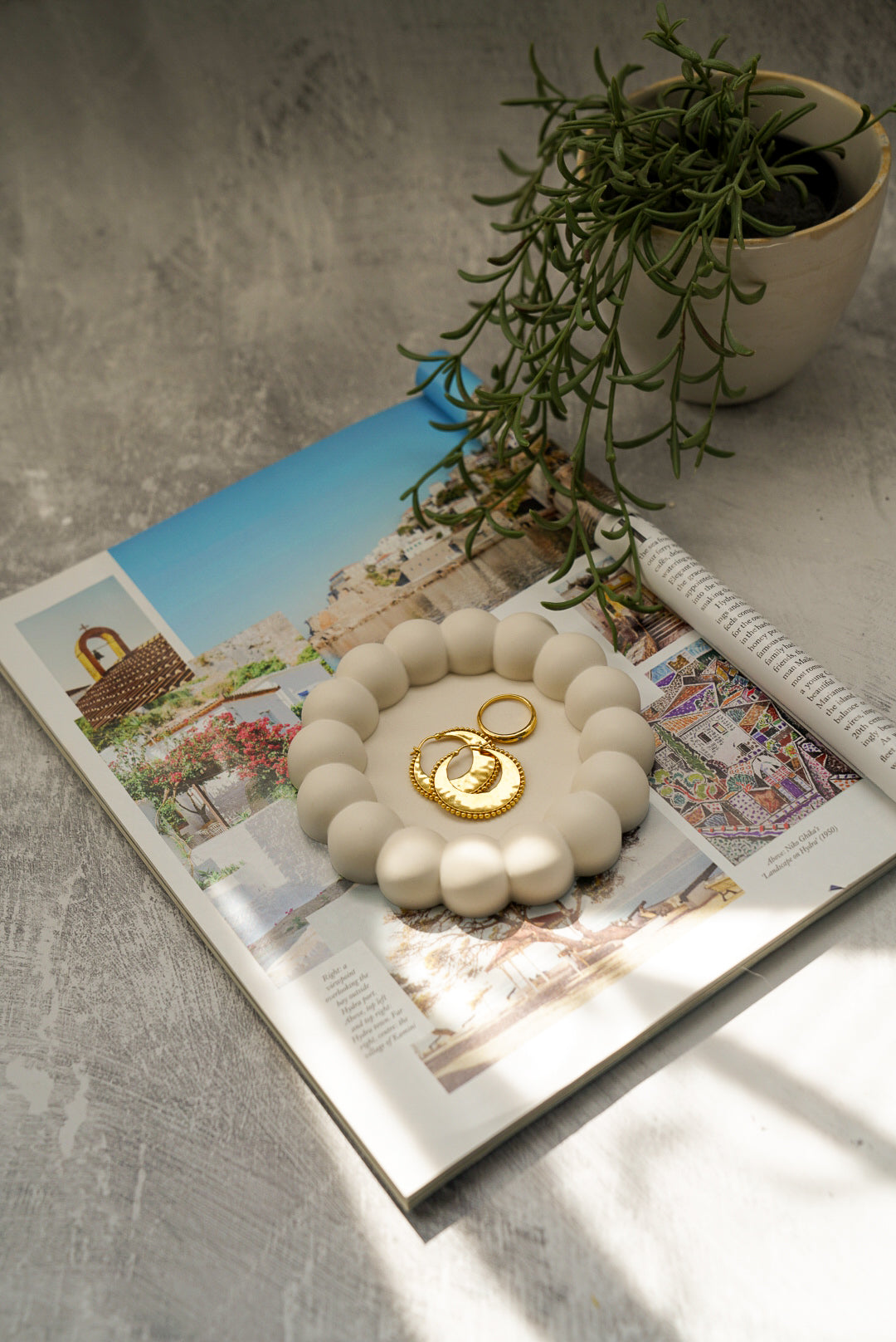 Bubble Jewellery Holder with gold earrings on it sitting on the magazine green plants on the side on a grey background 