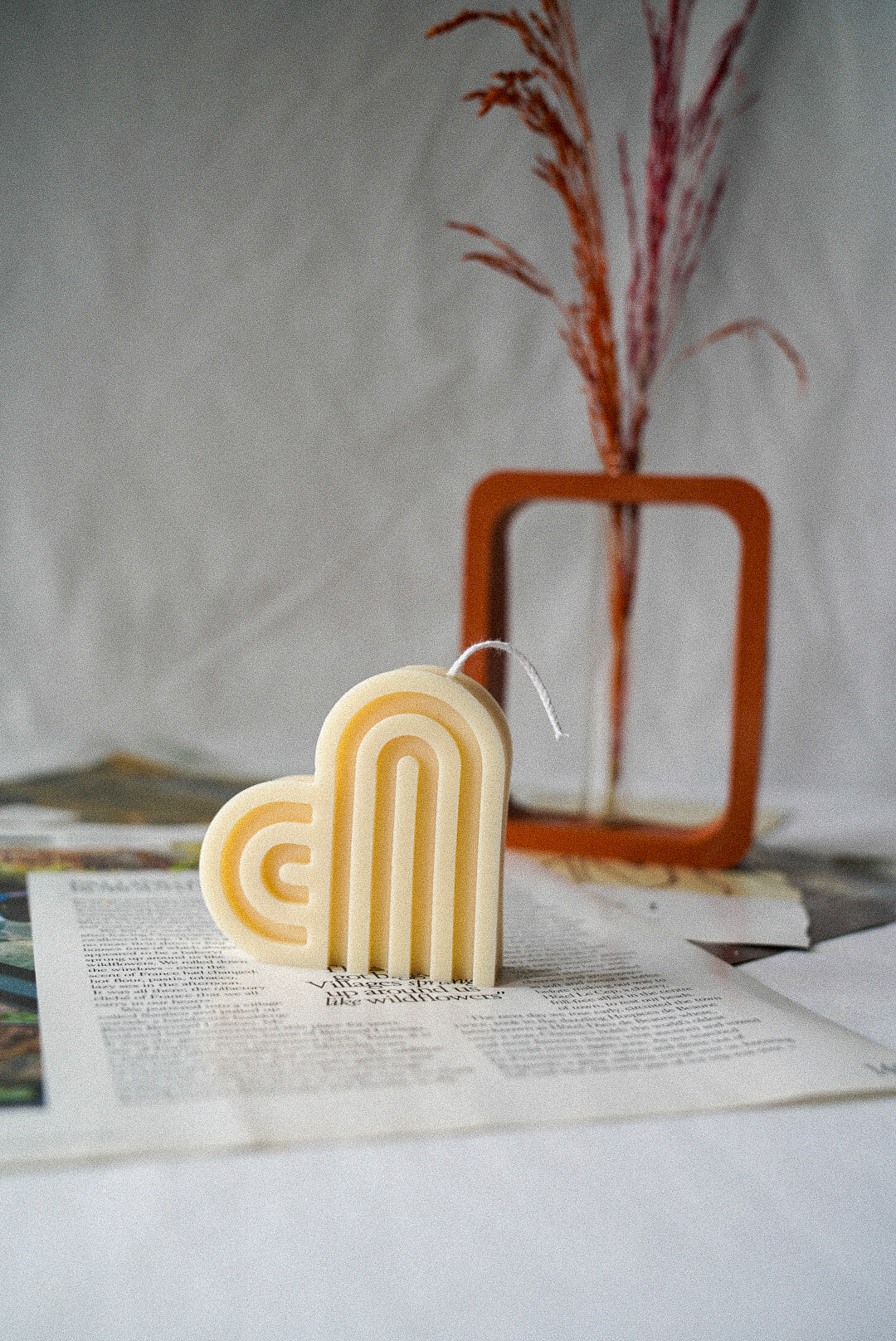 Heart-Shaped Soy Wax Candle on a magazine with rectangular vase on the background. 