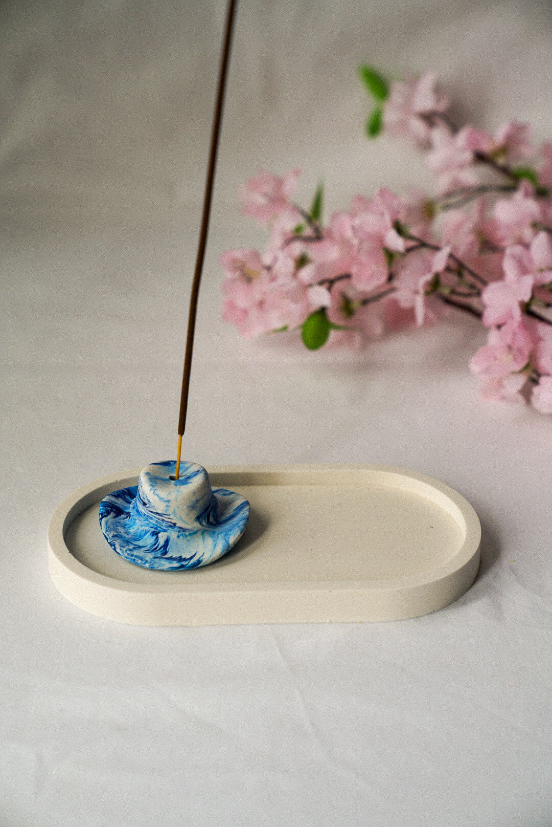 Marble blue Cowboy Hat Incense Holder with incense in it sitting on a trinket tray with flowers on the background.