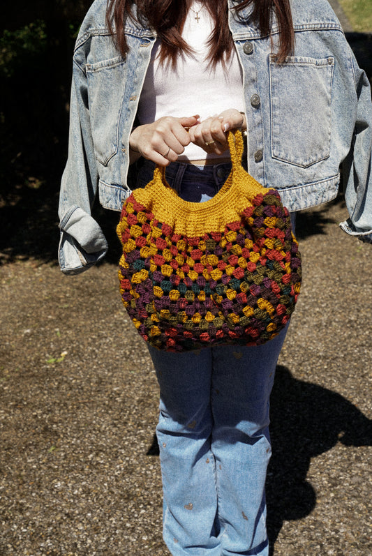 Holding a handmade colourful handbag.