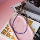 Pink silicone product with blue beaded necklace on a pink surface with magazine in background