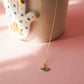 Necklace with a pendant on a pink surface next to a ceramic cup