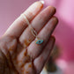 Hand holding a gold necklace with a blue eye pendant against a pink background