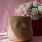 Beige female vase with a necklace draped over it on a pink surface with flowers in the background