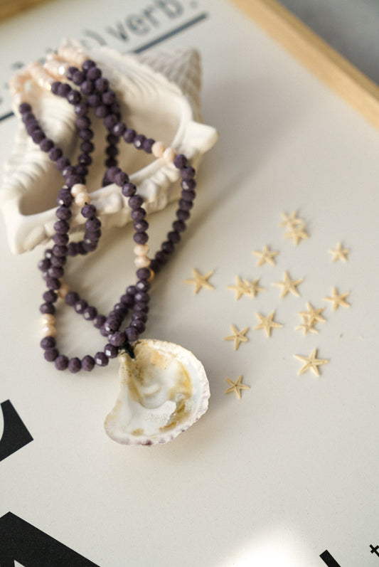 Necklace with purple beads and shell pendant on a decorative surface with star decorations