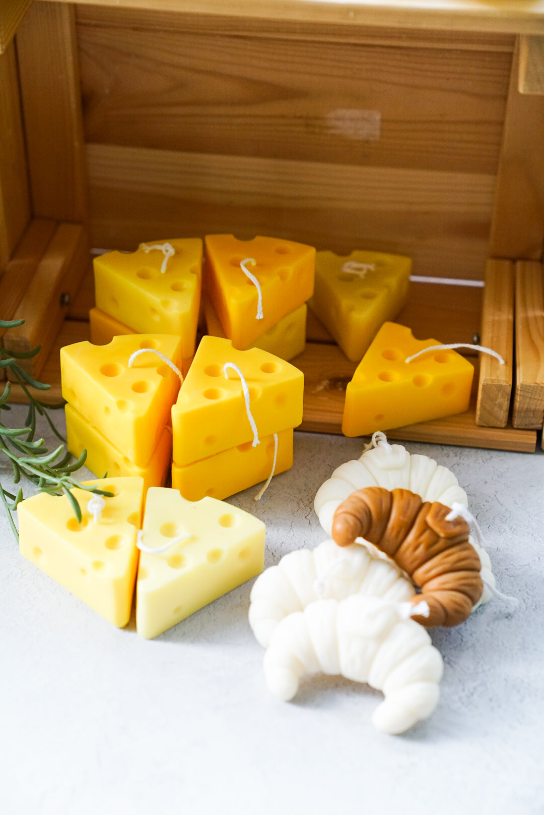 Cheese and croissant shaped soy wax candles are on the wooden box.