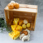 Cheese, croissant, lemon and orange shaped soy wax candles are on the wooden box with green plans on the side with a grey background.