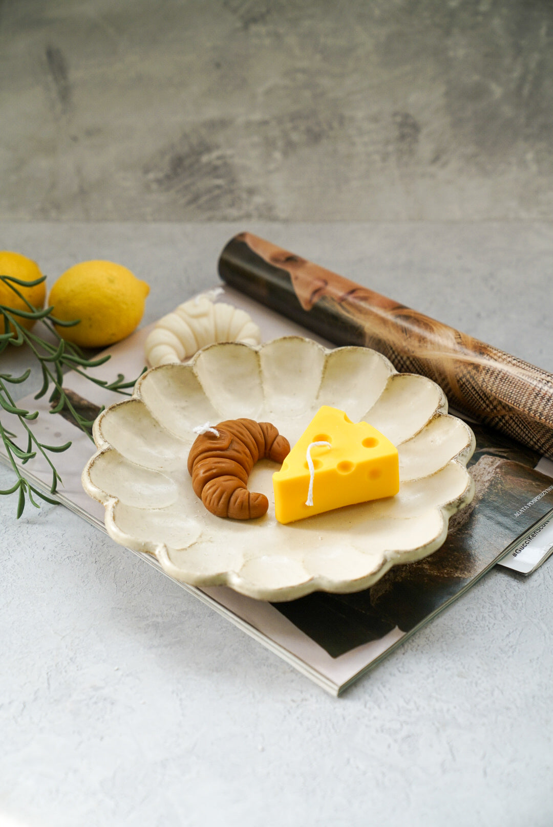 Cheese and croissant shaped candles are on a plate with lemons on the side