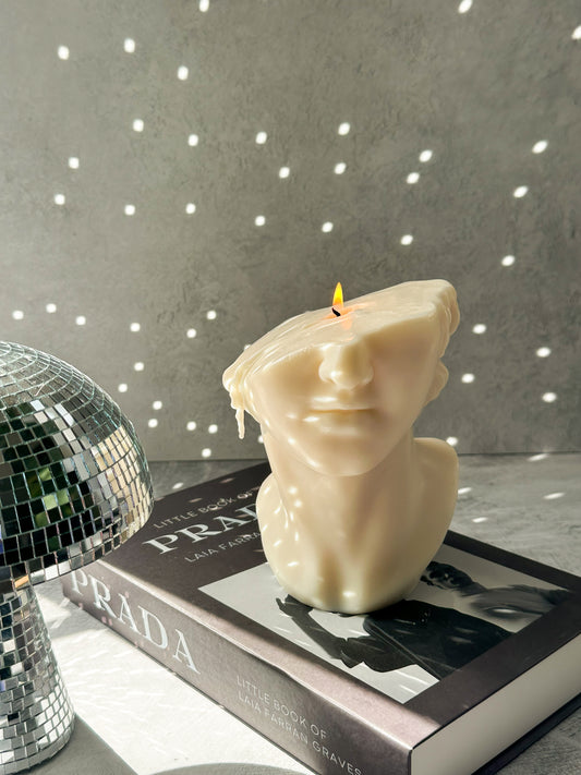 Burning Half David Head Statue Candle on a magazine and disco ball next to it.