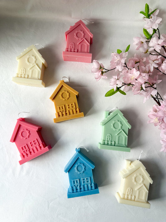 Colourful House Shaped Soy Wax Candles flowers next to them. 