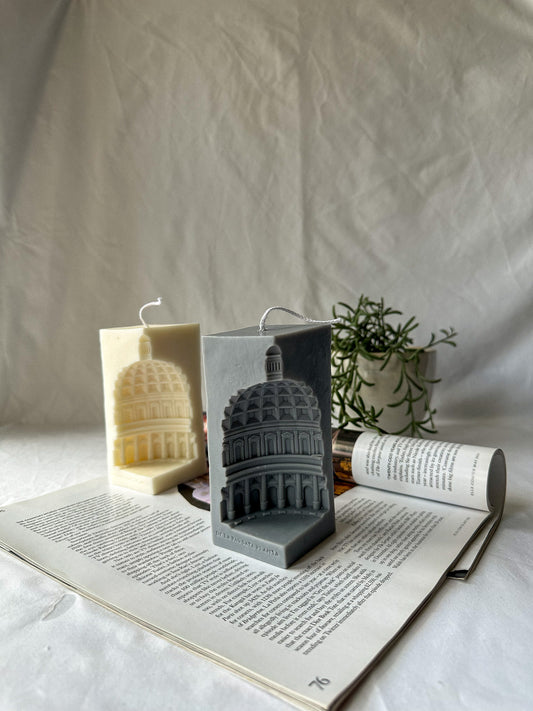 Ivory and Grey Rome Pantheon Capital Soy Candle on a magazine green plant on the background.