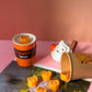 Cup with pumpkin spice flavor and small pumpkin decorations on a pink surface.