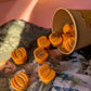 Pumpkin shaped wax melts spilling out of a paper cup onto a magazine with a blurred background